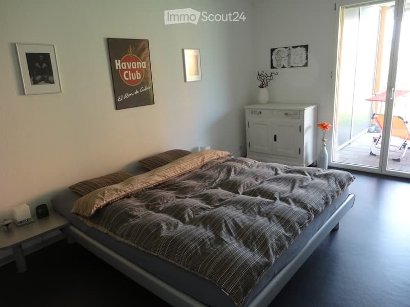 Bedroom with a large bed, nightstand, cabinet, and artwork on the walls. A sliding glass door leads to a balcony.