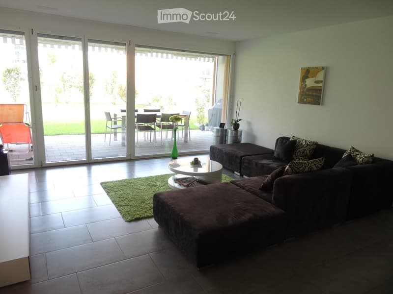 Modern living room with large sliding glass doors leading to a patio, a dark brown sectional sofa with patterned cushions, a white coffee table, a green shag rug, and a dining area visible through the doors.