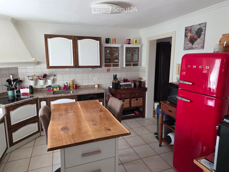 The kitchen features a wooden dining table with chairs, a red refrigerator, microwave, cabinets, and a kitchen island with a sink and various kitchen utensils.