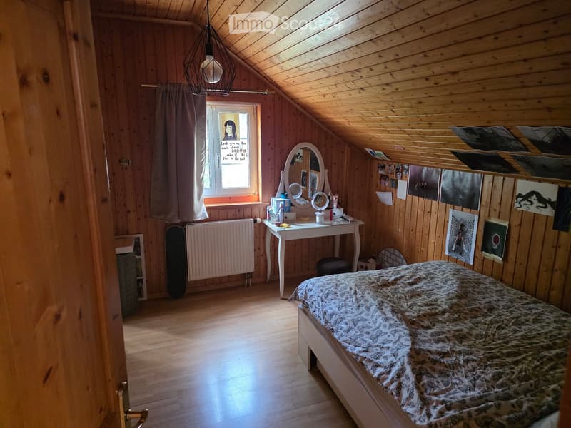 Cozy attic bedroom with wooden walls and slanted ceiling, featuring a bed, desk, mirror, radiator, and skateboard.