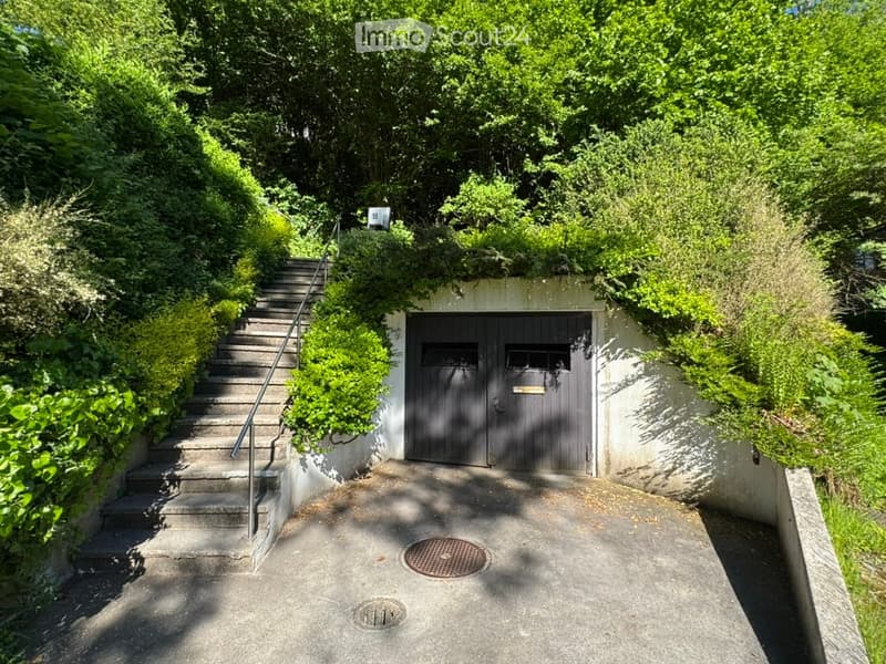A modern garage with a concrete staircase leading up to it, surrounded by lush greenery.