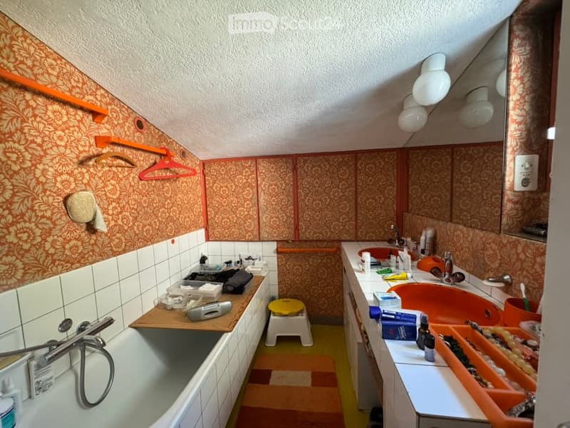 Bathroom with orange and white patterned tiles, a bathtub, sink, mirror, and various toiletries on the counter.