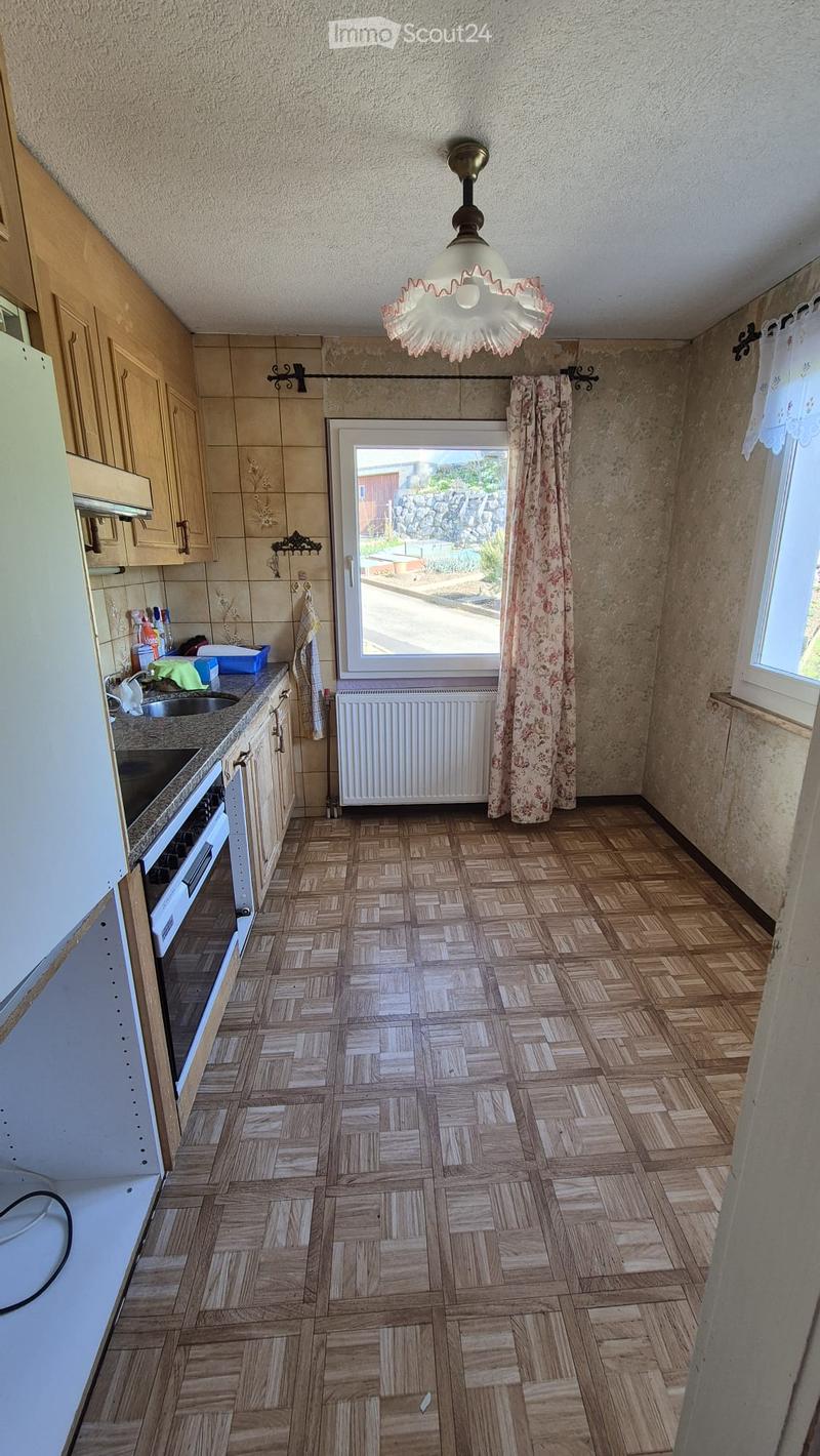 Kitchen with wooden herringbone flooring, light wooden cabinets, a white oven, a sink, a radiator, and a floral curtain on the window.