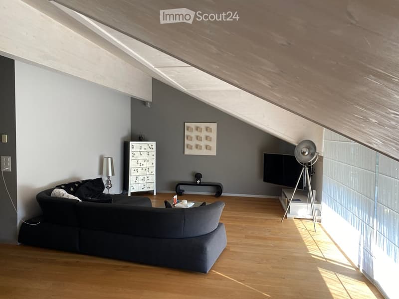 raised ground floor living room with a U-shaped sofa, a TV, a cabinet, a small table, a lamp, a tripod, a large glass window, and a power outlet.