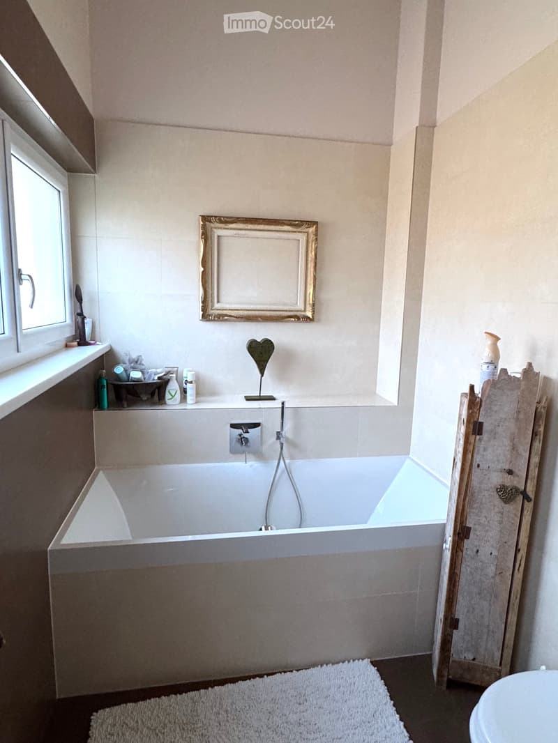 Bathroom with a bathtub, toilet, wooden cabinet, and framed picture.
