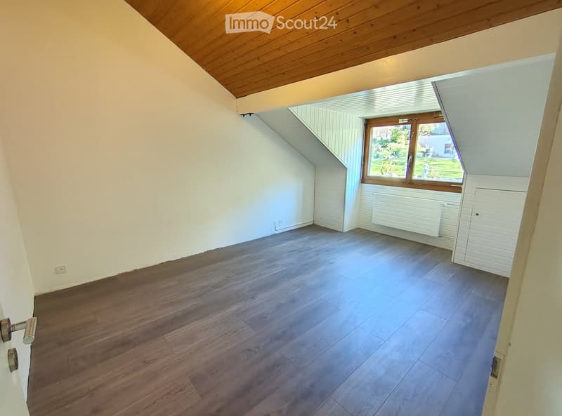 Empty attic room with wooden flooring, white walls, and a skylight window offering a view of the garden.