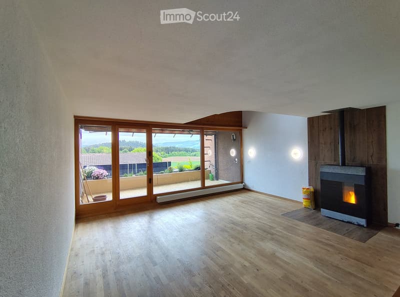 Modern living room with wooden flooring, large sliding glass doors leading to a balcony, and a fireplace with a burning fire.