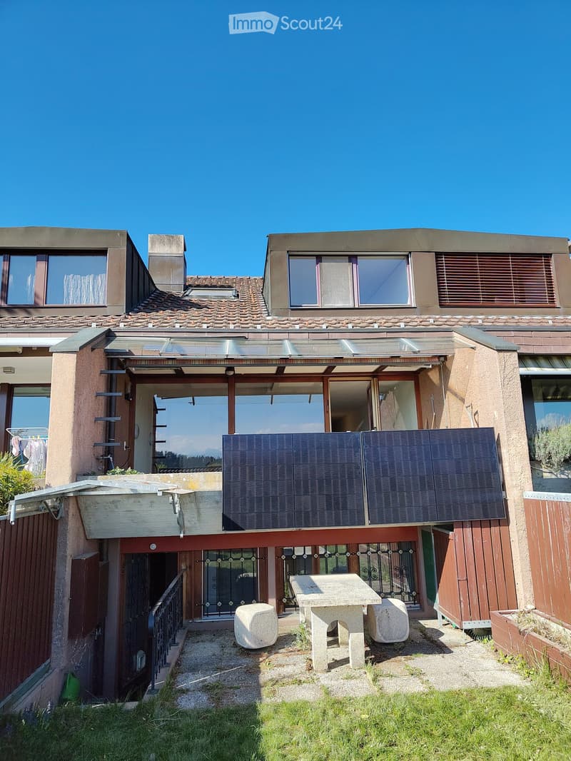 Two-story house with a tiled roof, solar panels on the roof, and a small outdoor seating area with a stone table and chairs.