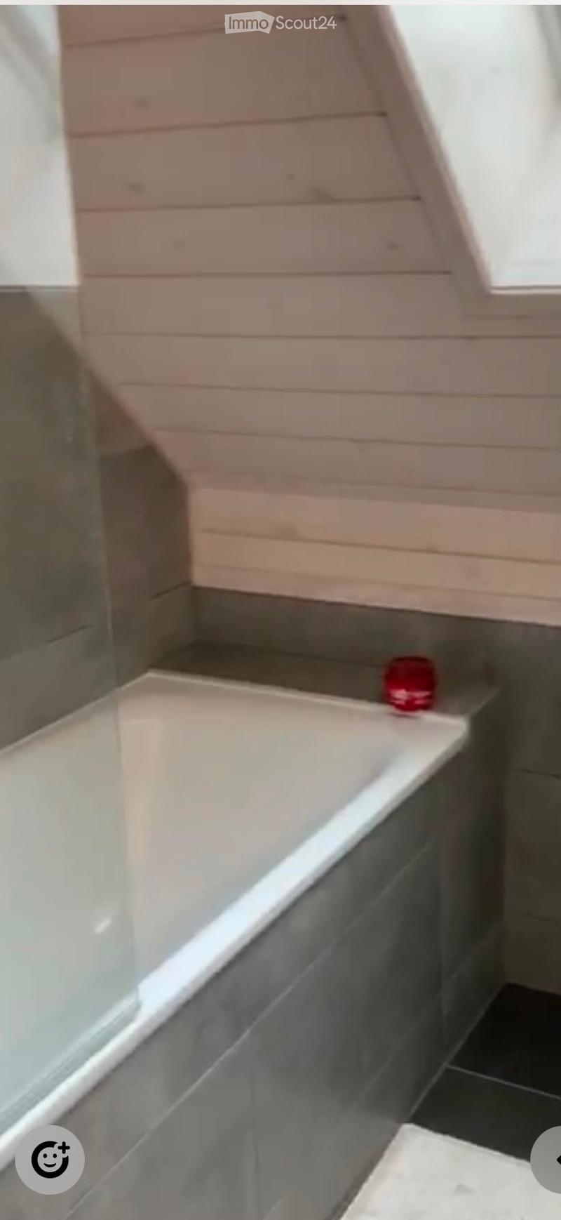 Modern bathroom with a white bathtub, tiled walls, and a glass shower enclosure. The walls are painted in a light wood finish, and the floor is tiled.