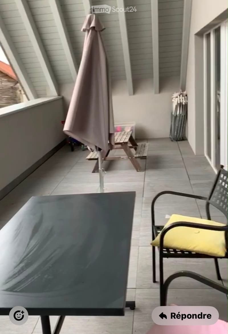 Balcony with tiled floor, a black table, a yellow chair, and a folded umbrella.