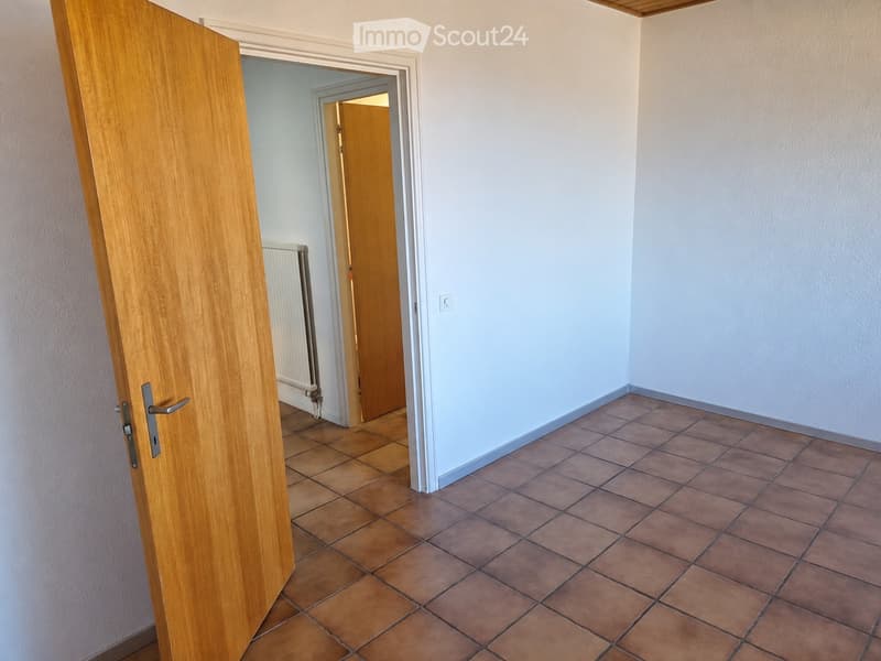 Empty room with tiled floor, light-colored walls, and an open wooden door leading to another room.