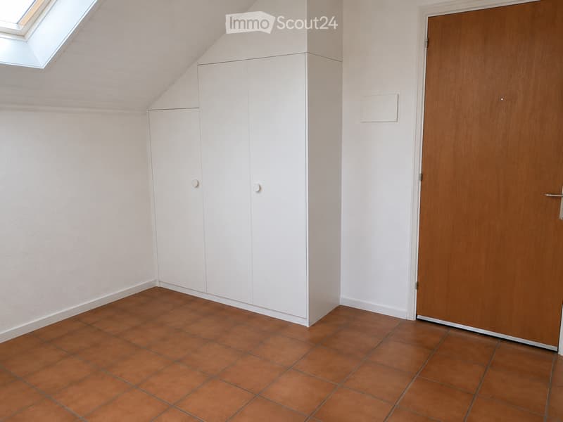 Empty room with white walls, brown tiled floor, white built-in closet, and a wooden door.