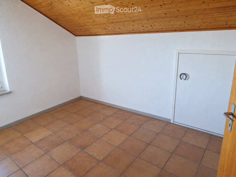 Empty room with tiled floor, white walls, wooden ceiling, and a closed door.