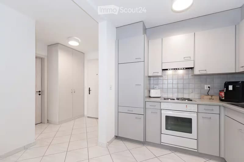 Modern kitchen with white cabinets, stainless steel appliances, and tiled flooring.