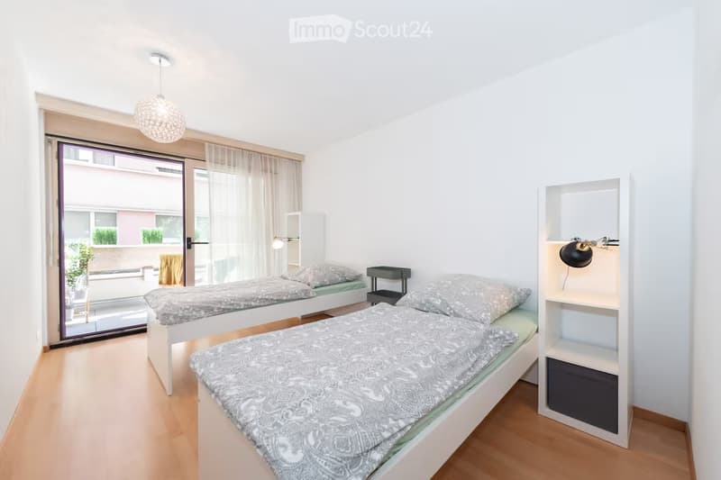 Bright bedroom with two single beds, nightstand, shelf, and modern lighting.