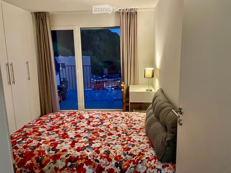 Cozy bedroom with a large bed, nightstand, lamp, and a view of a balcony or terrace area.