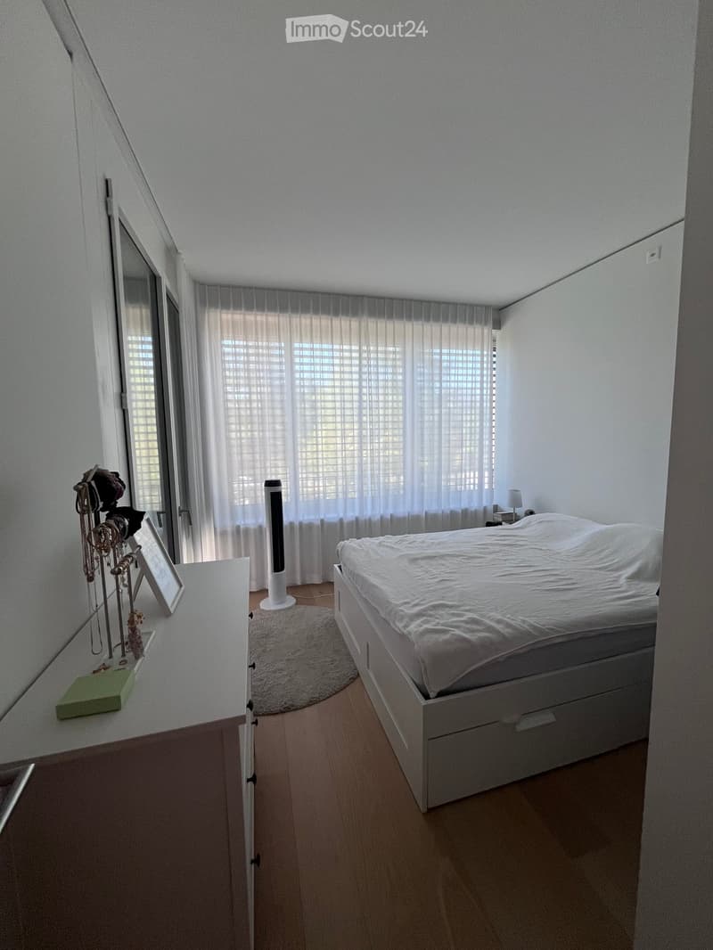 Modern bedroom with a white bed, nightstand, fan, mirror, and a small table with decorative items.