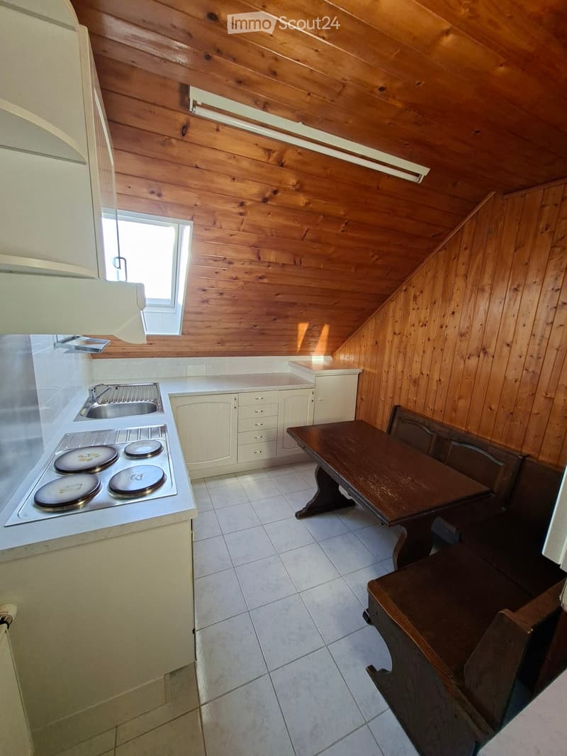 Cozy kitchen with wooden walls and ceiling, featuring a stove, sink, cabinets, and a small dining table with chairs.