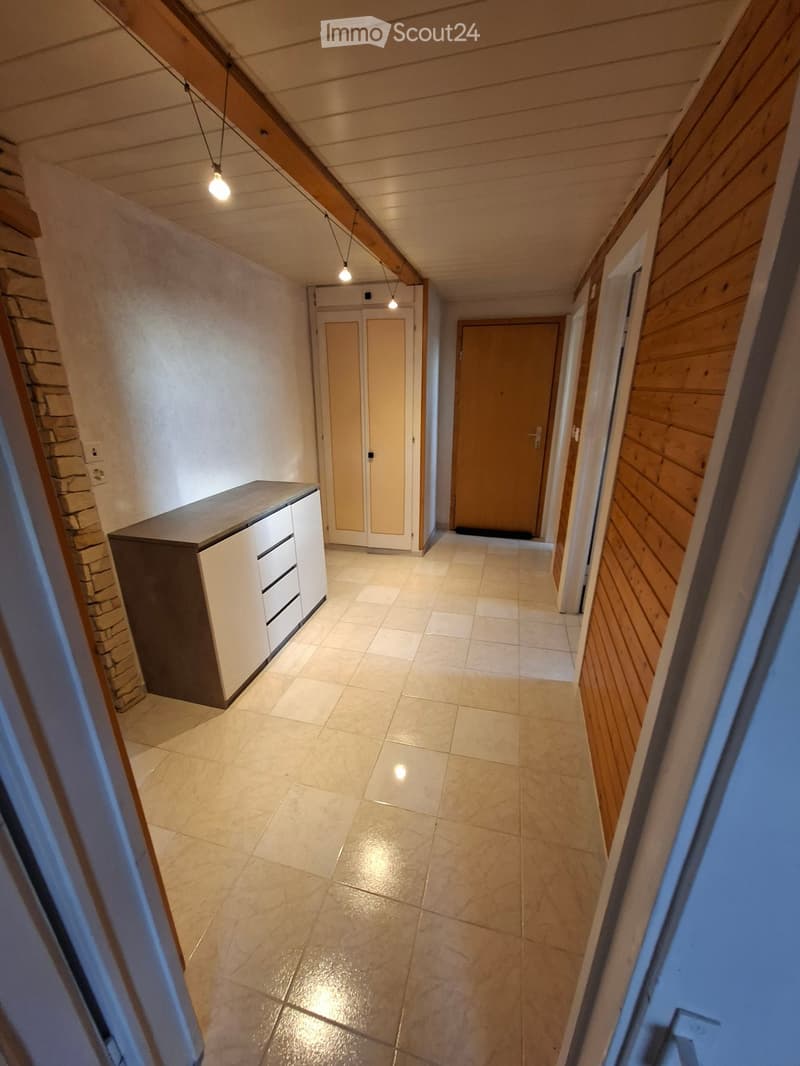 Empty hallway with tiled floor, wooden walls, and built-in storage unit on the left side.