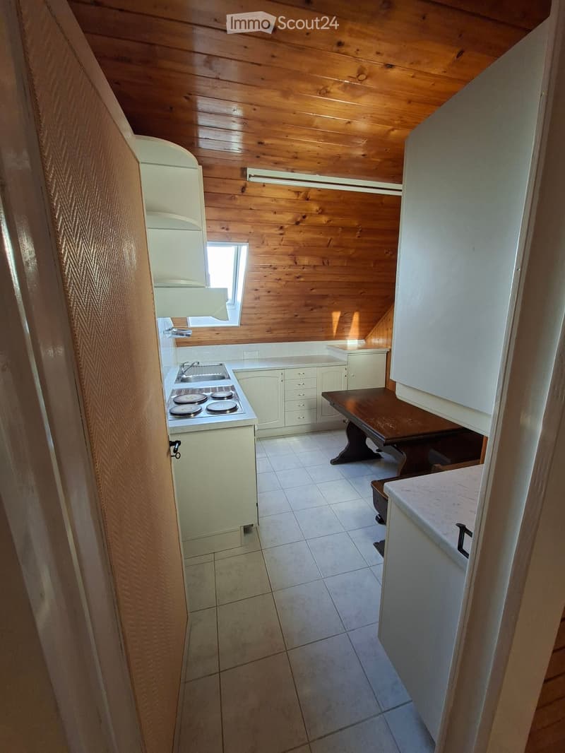 Compact kitchen with white cabinets, a four-burner stove, a sink, a refrigerator, and a small wooden table.