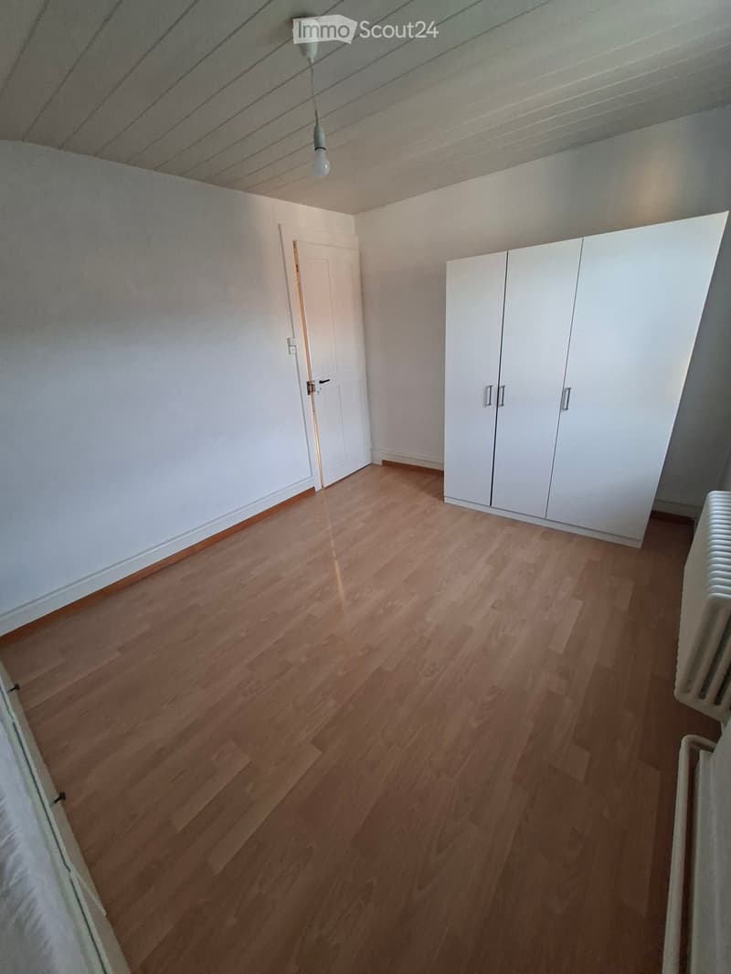 Empty room with wooden flooring, white walls, a white closet, and a door leading to another space.