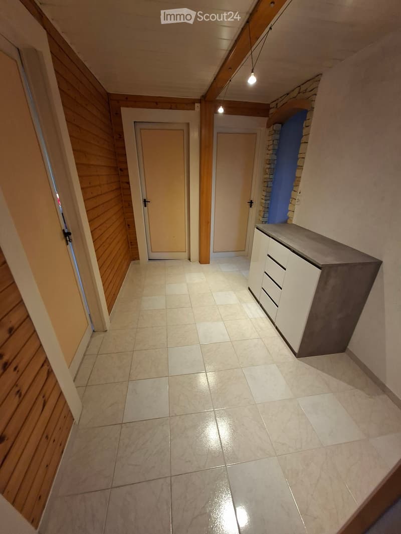 A narrow hallway with tiled flooring, wooden paneling on one side, and white cabinetry on the other. Two doors are visible, one on each side of the hallway.