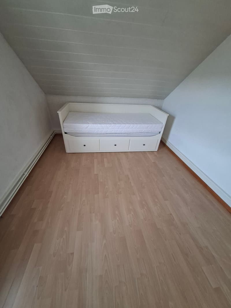A small, furnished room with a single white sofa bed and wooden flooring.