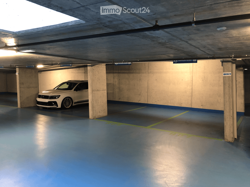 Underground parking area with a single white car parked, concrete pillars, blue floor, and green markings.