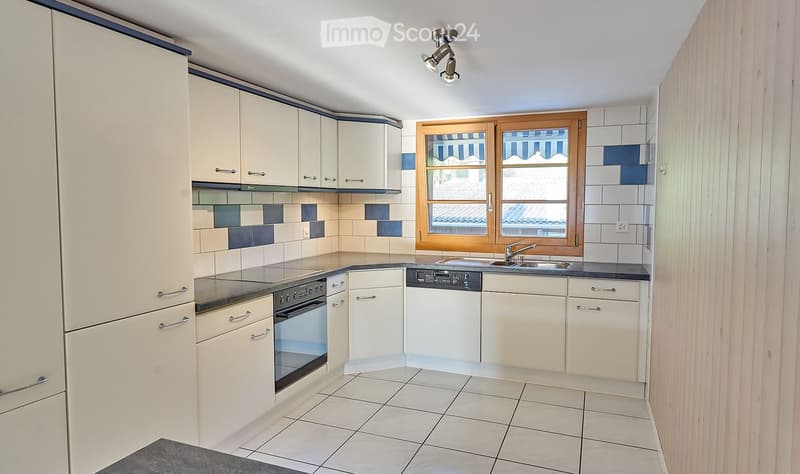 Modern kitchen with white cabinets, stainless steel appliances, tiled backsplash, and a window with wooden frame.
