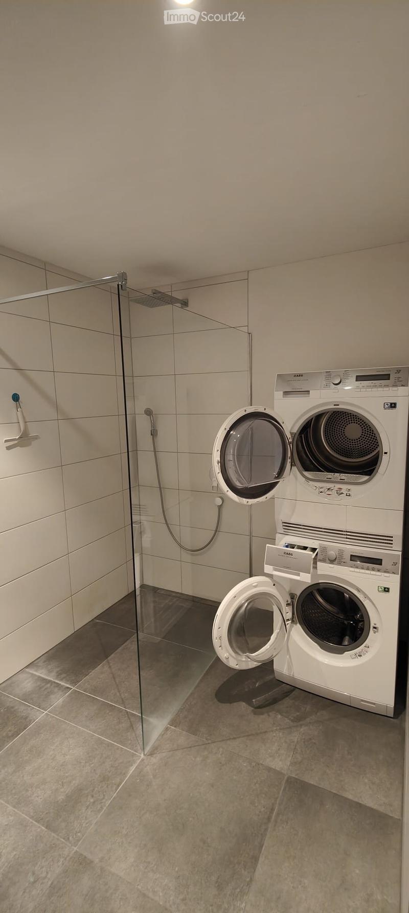 Shower area with tiled floor, white tiled walls, glass shower enclosure, washing machine, dishwasher.