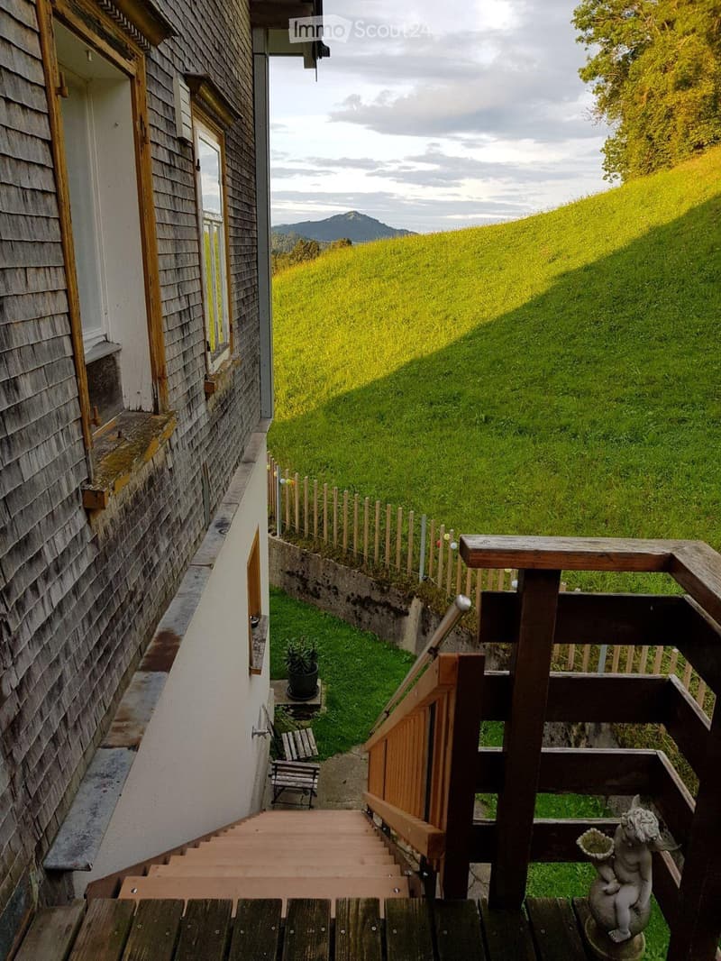 Wooden staircase leading up to a raised wooden deck, with a small bench, a statue, and a potted plant on the hillside.