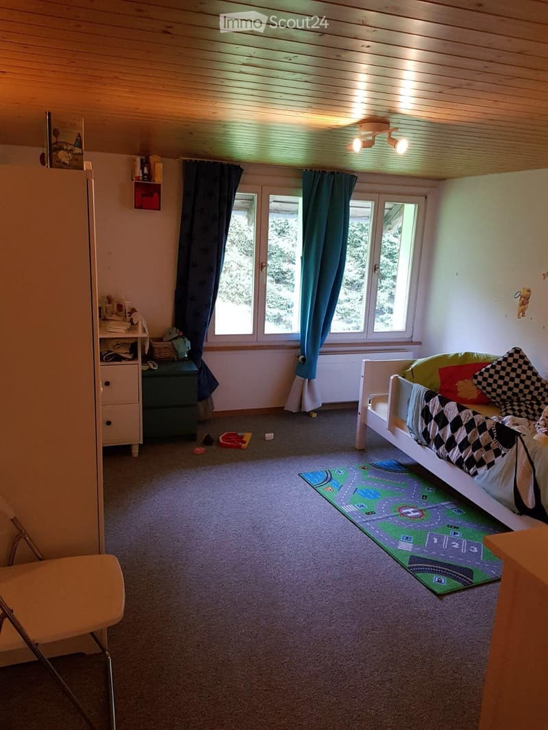 A cozy bedroom with a single bed, colorful pillows, a wardrobe, a chair, and a play mat on the floor.