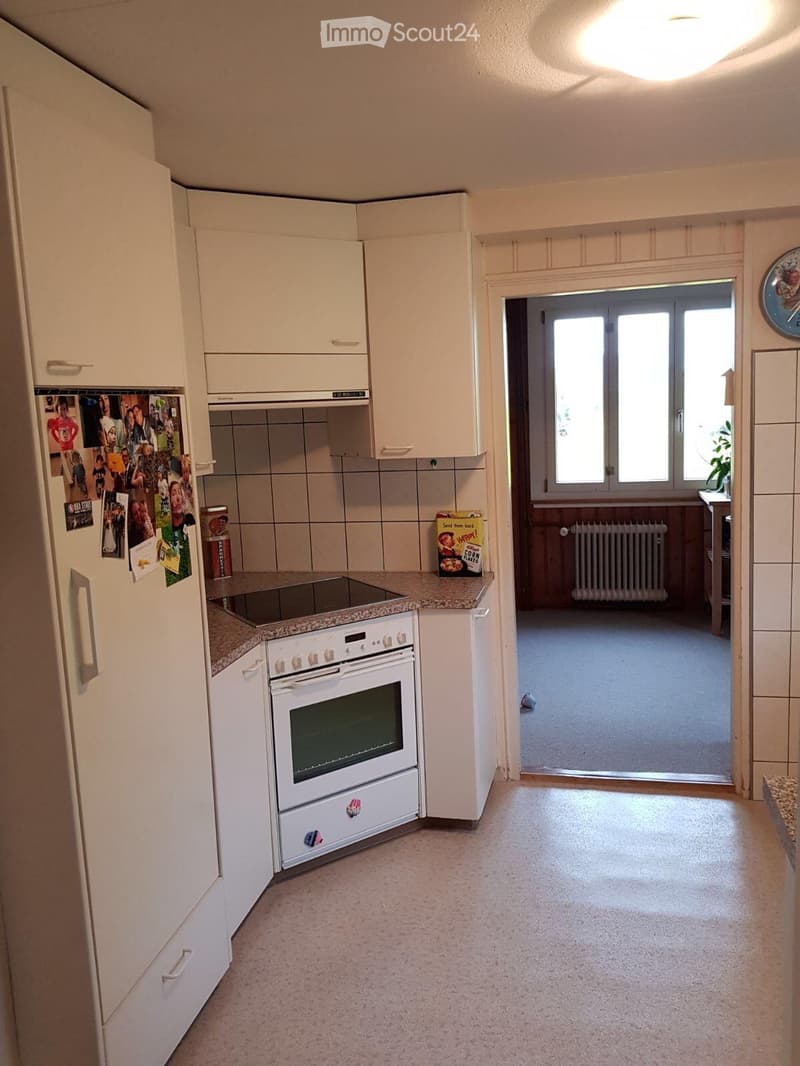 Modern kitchen with white cabinets, a refrigerator with photos, an oven, and an induction cooktop. The floor is tiled, and there is a doorway leading to another room.