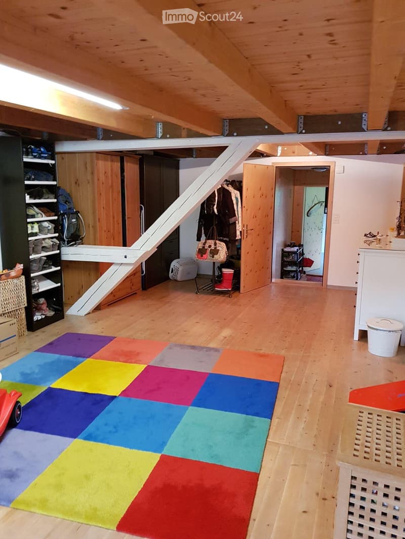 Bright, wooden-floored room with a colorful play mat, staircase leading to another level, shelves with shoes and bags, and various storage items.