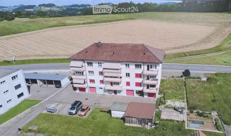 Multi-story residential building with balconies, garage, and parking area.