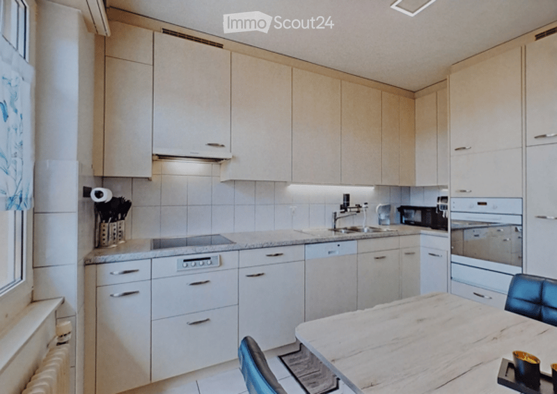 Modern kitchen with light wood cabinets, stainless steel appliances, and a marble dining table with chairs.