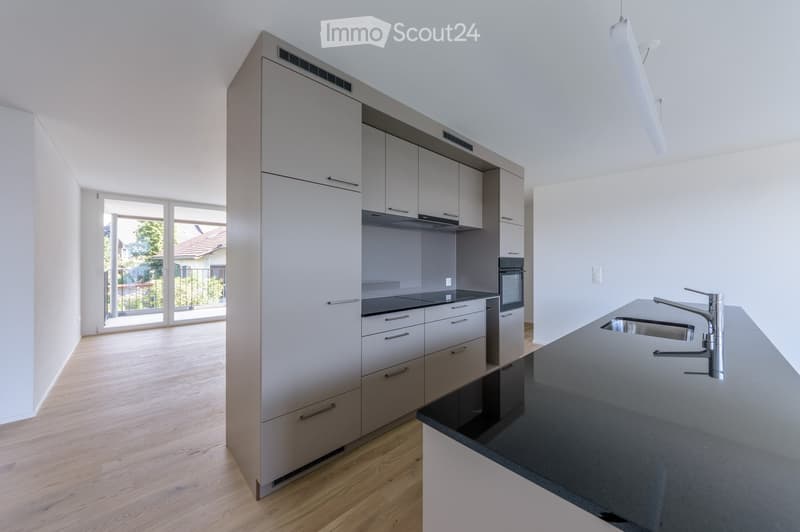 Modern kitchen with light grey cabinets, a central island, and a black countertop. Features a sink with a modern faucet, an oven, and a stove.