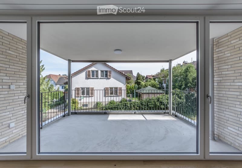 Modern balcony with large glass doors, metal railing, concrete floor, and view of neighboring houses and greenery.