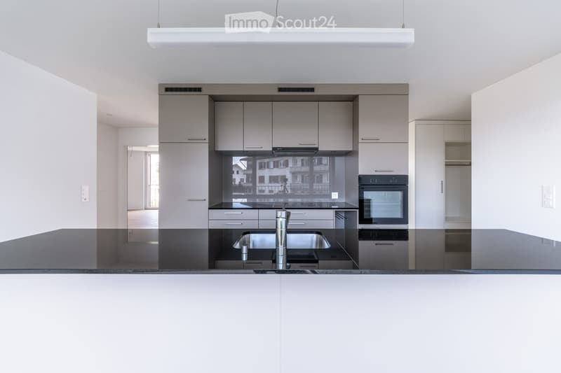 Modern kitchen with white cabinets, stainless steel sink and faucet, built-in oven, and sleek countertops.