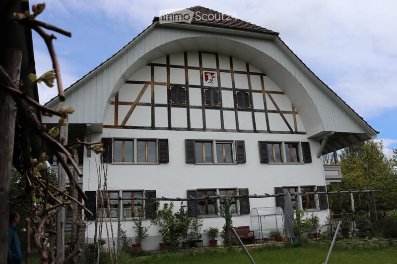 white house, red and white emblem, arched windows, sloped roof, black shutters, lush garden, potted plants, fence