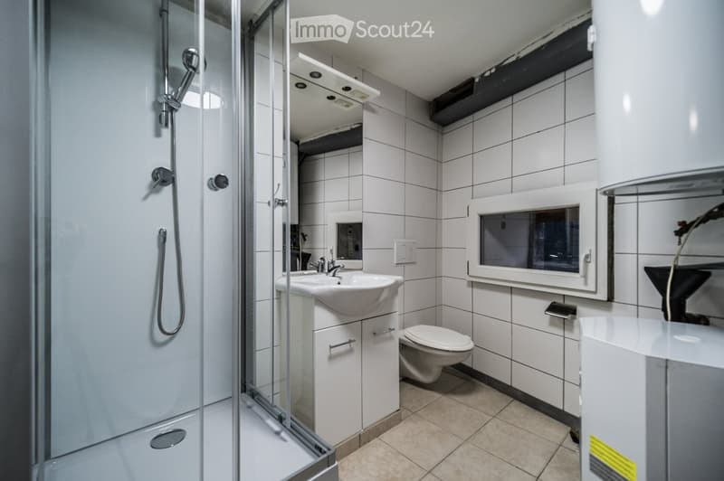 Modern bathroom with white tiles, a glass-enclosed shower, a sink with a cabinet, and a toilet.