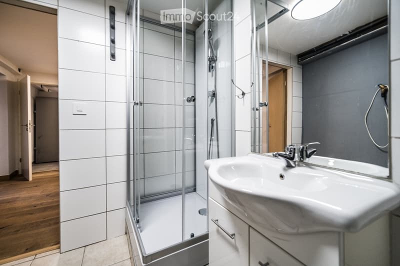 Modern bathroom with white tiles, a glass-enclosed shower, a white sink with a chrome faucet, and white cabinets.