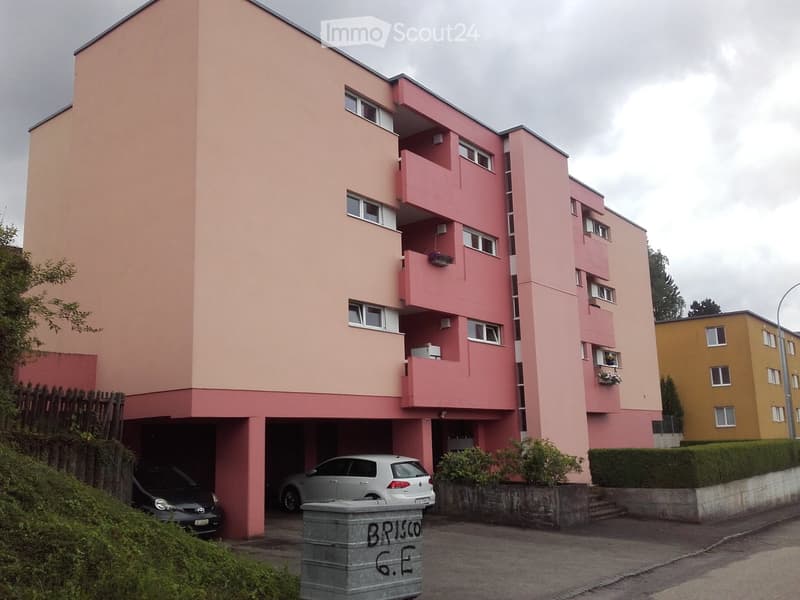 Pink multi-story apartment building with balconies, garage, and parked cars.