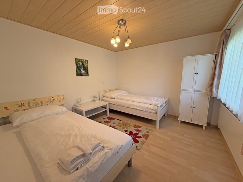 Cozy bedroom with two single beds, nightstand, cabinet, and a picture frame on the wall.