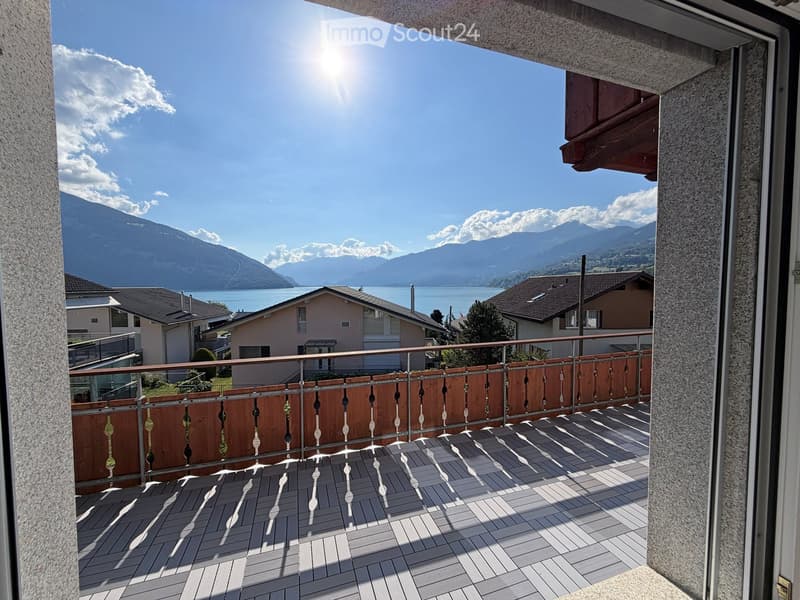 Balcony with wooden decking, metal railing, and scenic mountain and lake view.