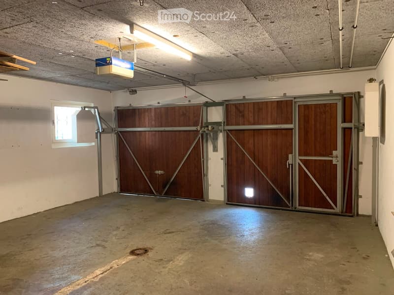 Empty garage with concrete floor, white walls, large wooden garage doors, and a small window on the left side.
