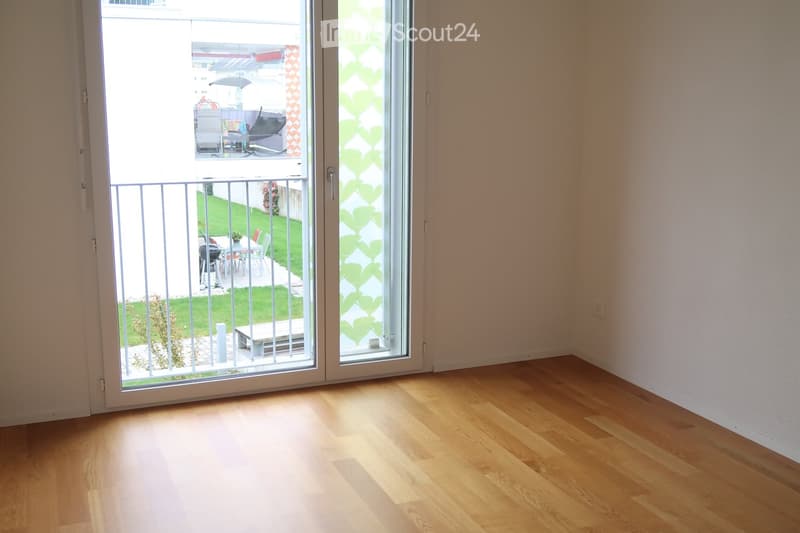 Empty room with wooden flooring and large sliding glass doors leading to a balcony and outdoor area.