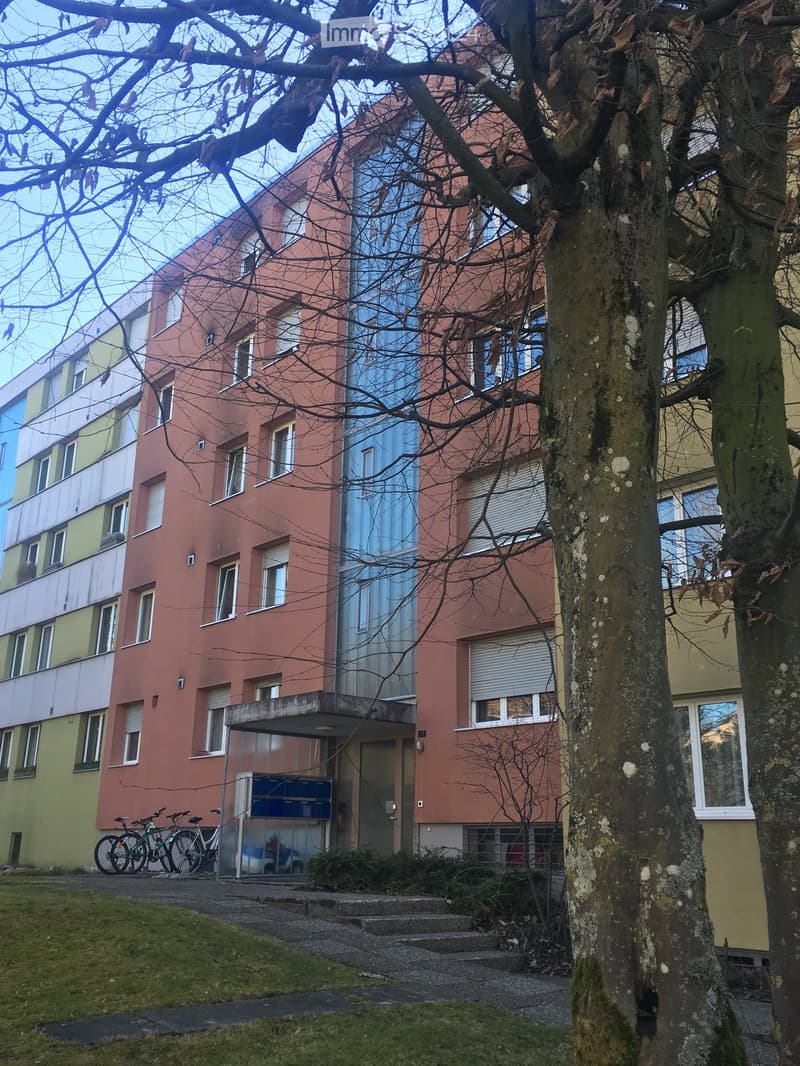 Multi-story residential building with colorful facades, windows, and a small entrance area with bicycles parked nearby.