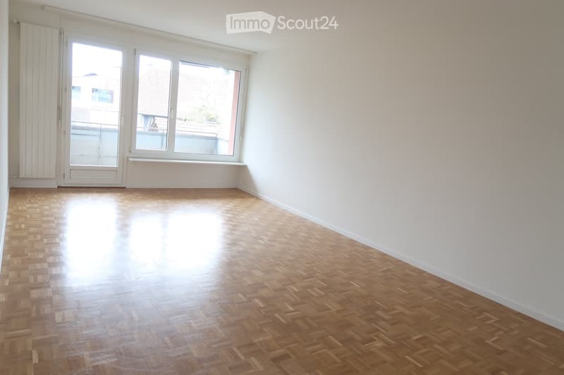 Empty room with wooden parquet flooring, white walls, large windows, and a door leading to a balcony.