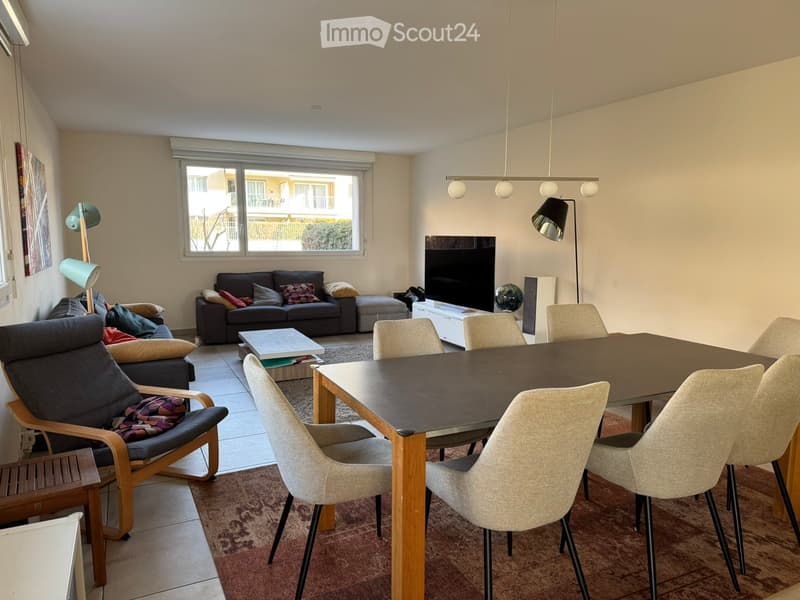 Bright living and dining area with a sofa, armchair, coffee table, dining table with chairs, TV, and decorative globe.